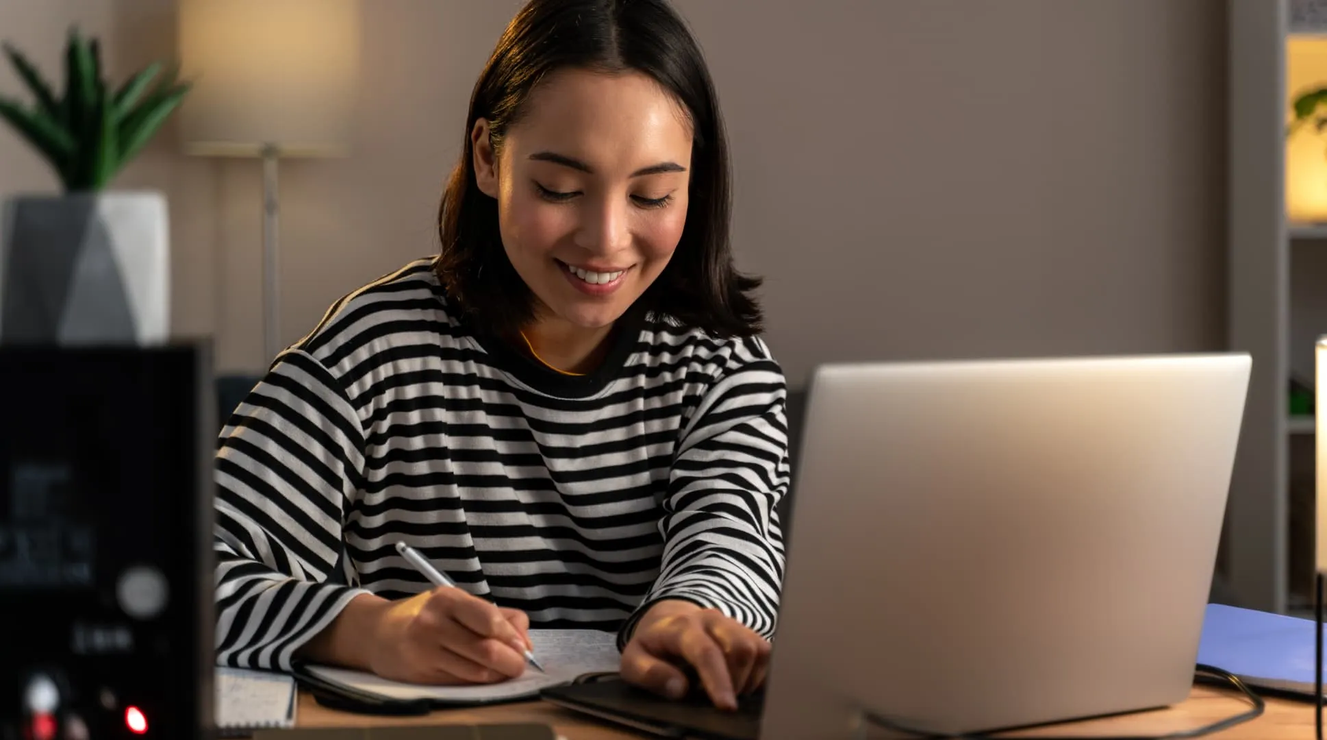 Student writing in a notebook while studying with a laptop